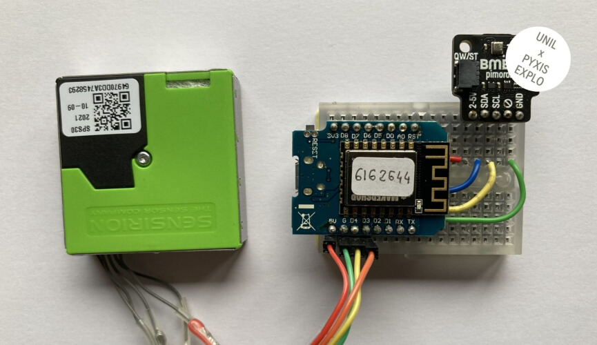 Deux dispositifs électroniques placés côte à côte sur une surface blanche. À gauche, un capteur vert de marque Sensirion avec un code QR visible. À droite, une carte électronique avec des fils de connexion colorés et un petit module, avec l'inscription '6162644' sur une étiquette